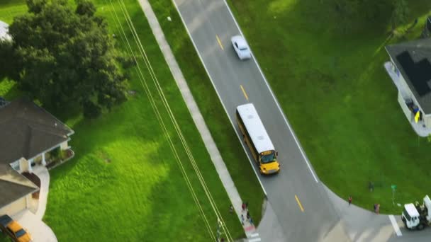早朝に子供たちをレッスンに迎えるために田舎街道を走る古典的なアメリカの黄色いスクールバスのトップビュー アメリカの公共交通機関 — ストック動画
