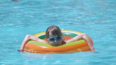 Mutlu kız çocuğu tropik tatiller sırasında güneşli yaz günlerinde yüzme havuzunda şişme çemberde yüzüyor..
