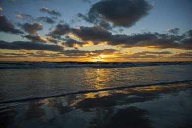 Gün batımında kumlu sahile vuran deniz suyu dalgalarının akşam manzarası.