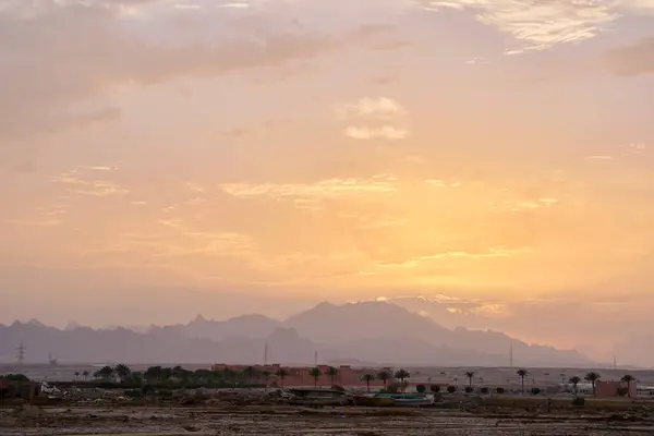 Sunset landscape with remote hotel complex against dark mountain peaks in egyptian desert.
