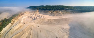 Kazı araçları ve çöp kamyonları ile inşaat endüstrisi için kireçtaşı malzemelerinin açık çukur madenciliğinin hava görüntüsü.