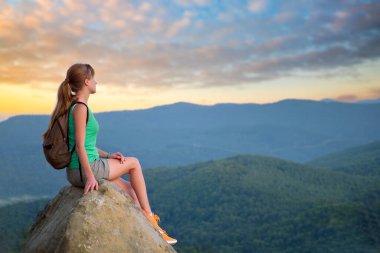 Kayalık dağ yamacında tek başına oturan kadın doğa manzarasının tadını çıkarıyor. Aktif yaşam konsepti.
