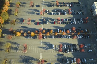 Aerial view of many colorful cars parked on parking lot with lines and markings for parking places and directions. Place for vehicles in front of a strip mall plaza.