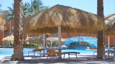 Boş güverte sandalyeleri, tropik tatil köylerinde havuz kenarında saman gölgesi şemsiyelerinin altında. Yaz tatilleri ve kaçış konsepti.