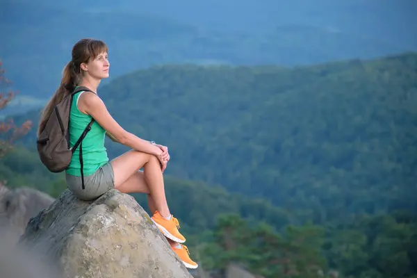 Hiker woman resting on rocky mountain top enjoying morning nature during her travel on wilderness trail. Lonely female traveler traversing high hilltop route. Healthy lifestyle concept.