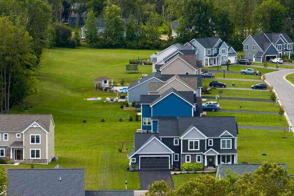 Low-density two story private homes in rural residential suburbs outside of Rochester, New York. Upscale suburban houses with large lot size and green grassy lawns in summer season.
