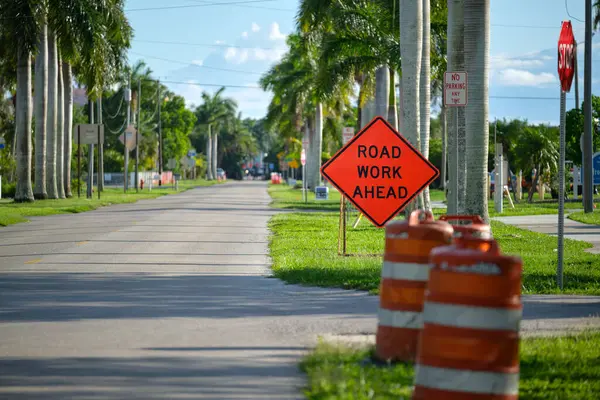 Road work ahead sign and barrier cones on street site as warning to cars about construction and utility works.
