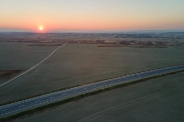 Asfalt yüzeyi ve akşamları beyaz işaretli boş şehirler arası yol manzarası.