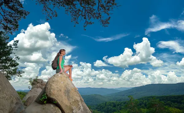 Hiker woman resting on rocky mountain top enjoying summer nature during her travel on wilderness trail. Lonely female traveler traversing high hilltop route. Healthy lifestyle concept.