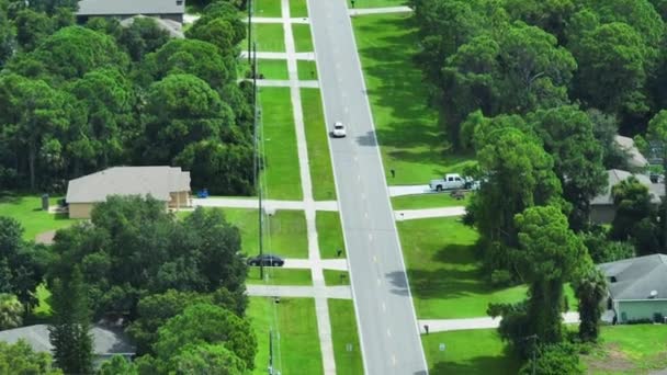 フロリダ州のアメリカの小さな町で交通車を運転する農村道路 静かな住宅街の緑の木と郊外の通りの間の私的な家 — ストック動画