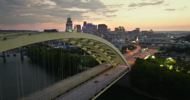シンシナティ市 オハイオ州 ダウンタウン地区の高速道路運転車を持つ 日没に明るく照らされた高い商業ビルを持つアメリカの都市のスカイライン — ストック動画