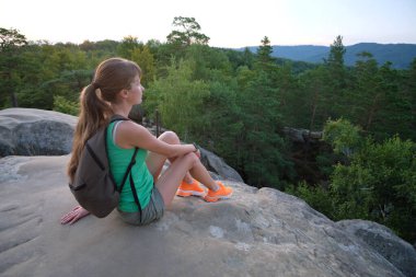 Young woman hiker sitting alone on rocky mountain enjoying view of evening nature on wilderness trail. Active way of life concept.