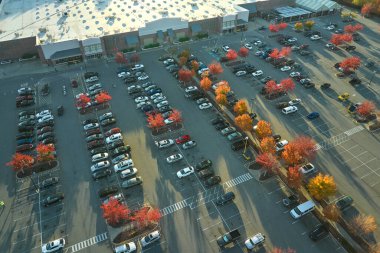 Hava manzaralı alışveriş merkezi ve park yerinde park yerleri ve yönler için çizgiler ve işaretler olan bir sürü renkli araba. Bir alışveriş merkezinin önünde araçlar için yer.