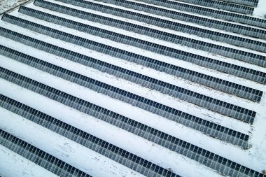 Aerial view of sustainable electrical power plant with solar photovoltaic panels covered with snow in winter for producing clean energy. Concept of low effectivity of renewable electricity in north.