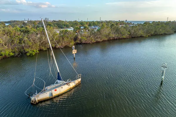 Capsized sunken sailing boat left forsaken on shallow bay waters after hurricane Ian in Manasota, Florida.