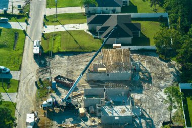 Florida 'nın banliyö bölgesinde inşaat halindeki ahşap çatı iskeleti yapısı olan bitmemiş bir ev üzerinde çalışan vinç ve inşaat işçilerinin hava görüntüsü..