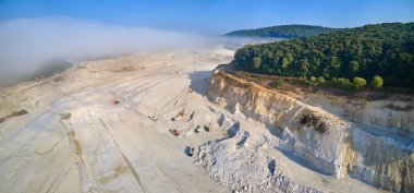 Kazı araçları ve çöp kamyonları ile inşaat endüstrisi için kireçtaşı malzemelerinin açık çukur madenciliğinin hava görüntüsü.
