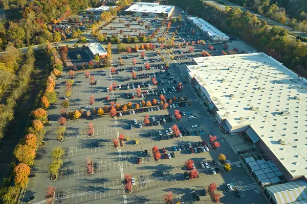 Bir alışveriş merkezinin önündeki otoparkta park edilmiş birçok arabanın üst görüntüsü. Tüketim ve piyasa ekonomisi kavramı.