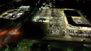 Parlak bir şekilde aydınlatılmış park yerindeki alışveriş merkezinin önüne park edilmiş arabalar. Tüketim ve piyasa ekonomisi kavramı.