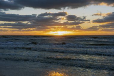 Gün batımında kumlu sahile vuran deniz suyu dalgalarının akşam manzarası.