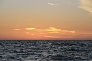 Dramatic bright red sky at ocean sunset, soft evening clouds over sea dark water.