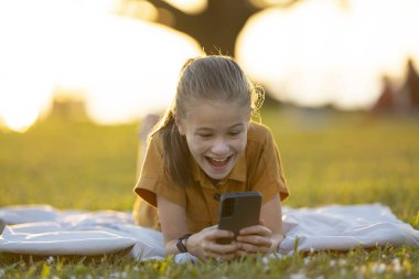 Bir arkadaşıyla yaz parkında cep telefonunda mesajlaşan pozitif kız..