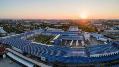 Akşamları yeşil ekolojik elektrik üretmek için endüstriyel binaların çatısına monte edilen mavi fotovoltaik güneş panellerinin hava görüntüsü. Sürdürülebilir enerji konsepti üretimi.
