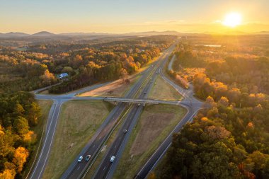 Elevated view of freeway exit junction over road lanes with fast moving traffic cars and trucks at sunrise. Interstate transportation infrastructure in USA.
