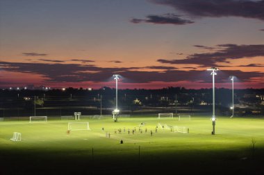 İnsanlar gün batımında halka açık stadyumda futbol oynuyorlar. Aktif yaşam konsepti.