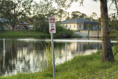 Florida parkında timsah olduğuna dair uyarı işareti. Rıhtım yakınlarında yürürken dikkat ve güvenlik.