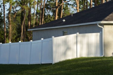 Bahçeyi çevreleyen yeşil çimlerde bahçe koruması ve mahremiyet için beyaz vinil çitler..