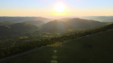 Tepenin tepesinde dönen toprak yol parlak batan güneşle aydınlanıyor. Vahşi dağlarda renkli günbatımının havadan görünüşü. Güzel doğa manzarası.