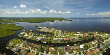 Florida yakınlarındaki deniz kıyısındaki uzak banliyölerdeki kırsal özel evlerin havadan görüntüsü körfez kıyısında yeşil bitki örtüsü olan sulak alanlar. Tropikal bölge kavramında doğaya yakın yaşamak.