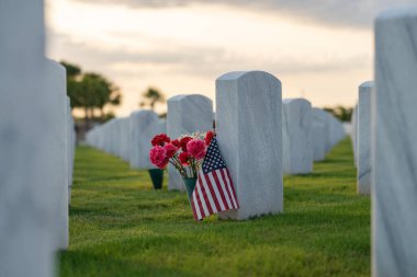 Amerikan ordusunun ulusal mezarlığı. Çiçeklerle süslenmiş beyaz mezar taşları ve yeşil çimlerde Amerikan bayrakları var. Anma Günü konsepti.