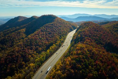 I-40 freeway road leading to Asheville in North Carolina thru Appalachian mountains with yellow fall forest and fast moving trucks and cars. Concept of high speed interstate transportation.