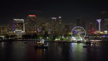 Biscayne Körfezi 'ndeki yansımaları ve şehrin finans merkezi Brickell' in aydınlatılmış gökdelenleriyle birlikte Bayside Pazarı 'ndaki Miami Gözlem Çarkı' nın gece manzarası..