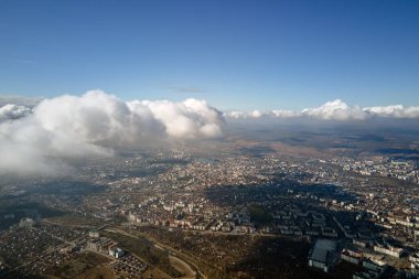 Uzak şehrin yüksek irtifasındaki uçak penceresinden hava manzarası beyaz kabarık kümülüs bulutlarıyla kaplı..