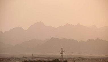 Sunset landscape with dark mountain peaks in egyptian desert and high voltage power lines.