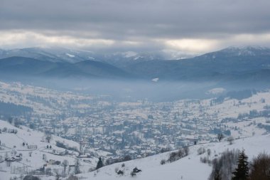 Soğuk dağlarda karla kaplı ormanlar arasındaki ücra yerleşim yerlerindeki küçük kır evleri ile kış manzarası.