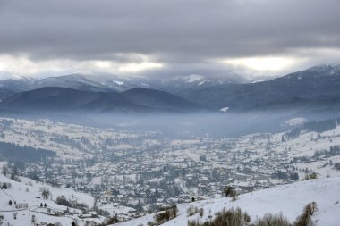 Soğuk dağlarda karla kaplı ormanlar arasında küçük köy evleri olan kış manzarası.