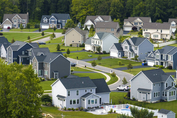 Low-density two story private homes in rural residential suburbs outside of Rochester, New York. Upscale suburban houses with large lot size and green grassy lawns in summer season.