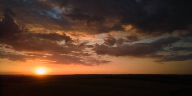 Parlak renkli günbatımı gökyüzü, batan güneş ve canlı bulutlar, karanlık manzaranın üzerinde..
