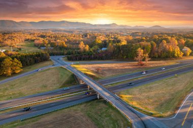 Freeway overpass junction with fast moving traffic cars and trucks in American rural area at sunset. Interstate transportation infrastructure in USA. clipart