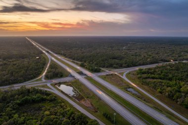 Elevated view of freeway exit junction over road lanes with fast moving traffic cars and trucks at sunrise. Interstate transportation infrastructure in USA.