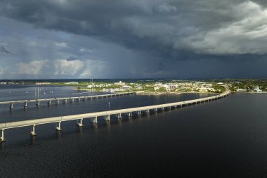 Stormy clouds forming from evaporating humidity of ocean water before thunderstorm over traffic bridge connecting Punta Gorda and Port Charlotte over Peace River. Bad weather conditions for driving. clipart