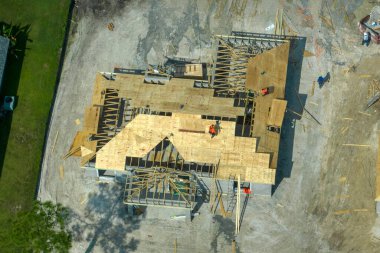 Florida 'nın banliyö bölgesinde inşaat halindeki ahşap çatı iskeleti yapısı olan bitmemiş bir ev üzerinde çalışan inşaatçıların hava görüntüsü..