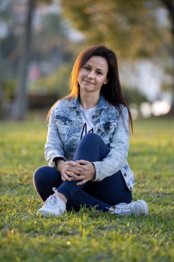 Şehir parkındaki yeşil otlakta dinlenen mutlu genç kadın..