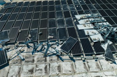 Yeşil ekolojik elektrik üretmek için endüstriyel yapı çatısına monte edilen rüzgar fotovoltaik güneş panellerinden hasar gören hava görüntüsü. Doğal afetin sonuçları..