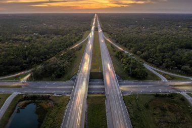 Elevated view of freeway exit junction over road lanes with fast moving traffic cars and trucks at sunrise. Interstate transportation infrastructure in USA.