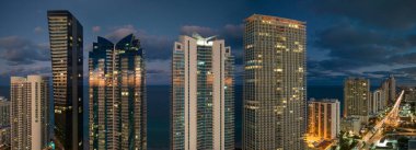 Florida, ABD 'deki Sunny Isles Beach şehrinin şehir merkezindeki gece şehir manzarası. Modern Amerikan megapolis 'indeki parlak gökdelen binalarıyla gökdelenler..